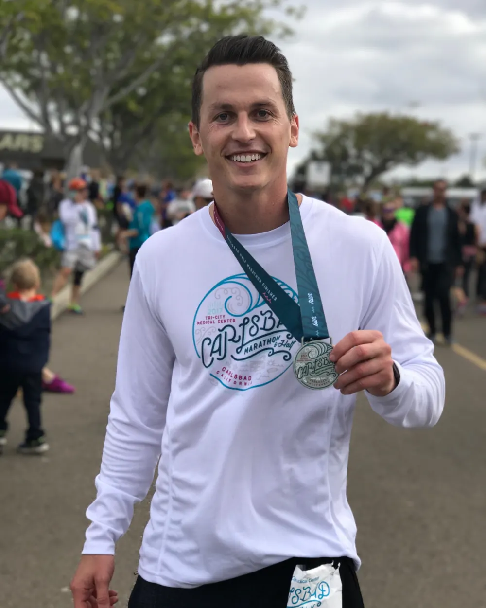 Alex at the finish of the Carlsbad half marathon, holding up the finisher medal