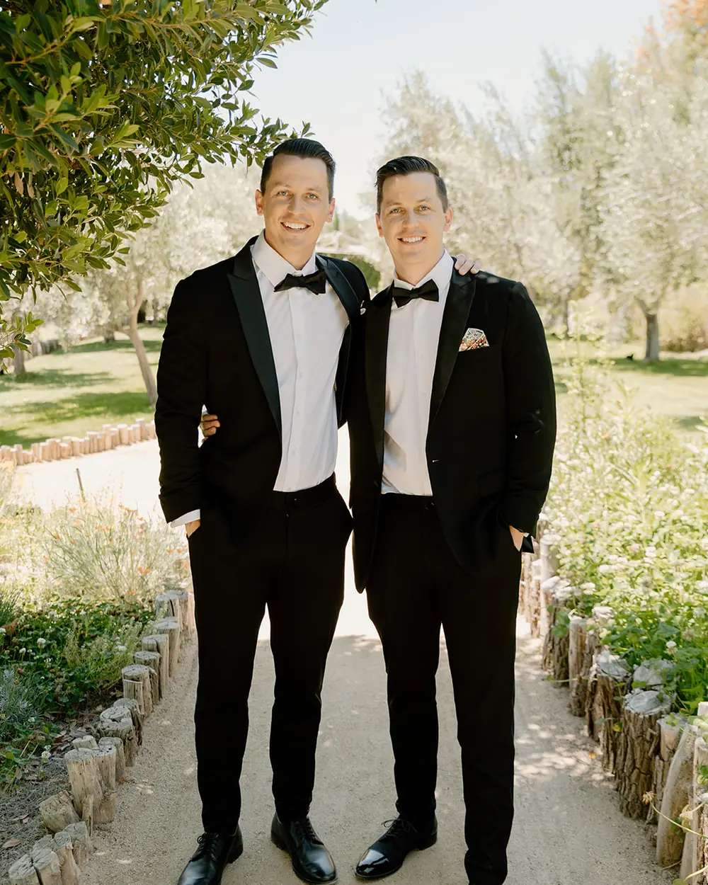 Alex and his twin brother in black tie, side by side on a garden path